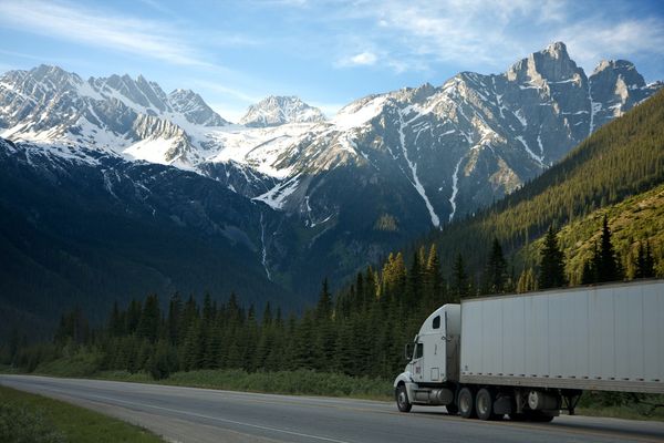 White tractor trailer driving up a road into the mountains