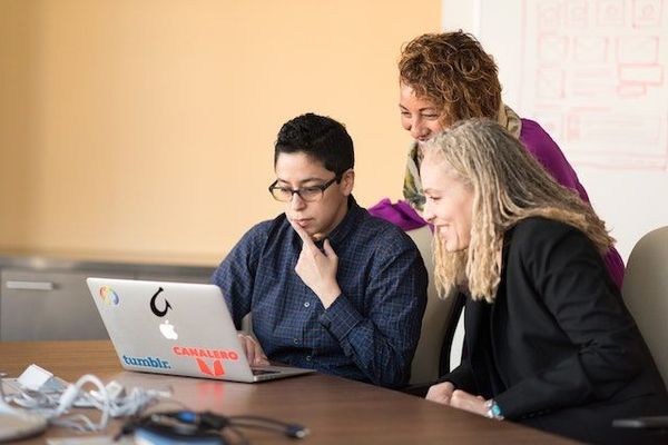 Three women hubbled around a laptop