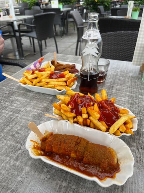 picture of table at fastfood restaurant. Food only. curryworst and fries and 1/2 empty soda bottle.